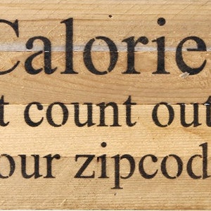 May include: Wooden sign with the text "Calories don't count outside your zipcode."