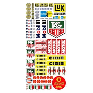 May include: A sheet of vintage racing car decals featuring logos for brands like Mobil, Tag Heuer, Motul, Cibie, Martini, Gulf, and Bosch. The decals are in various colors, including red, yellow, green, blue, and black.