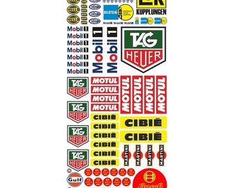 May include: A sheet of vintage racing car decals featuring logos for brands like Mobil, Tag Heuer, Motul, Cibie, Martini, Gulf, and Bosch. The decals are in various colors, including red, yellow, green, blue, and black.