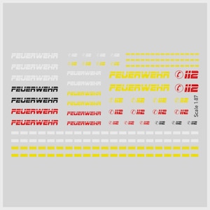 Könnte beinhalten: Ein Bogen mit Aufklebern mit dem Wort "FEUERWEHR" in verschiedenen Farben und Schriftarten, zusammen mit der Nummer "112" und einer Maßstabsanzeige. Die Aufkleber sind hauptsächlich weiß, gelb, rot und schwarz, geeignet für Modellfahrzeuge oder Bastelarbeiten.