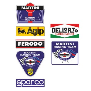Può includere: Una collezione di loghi di team di corse vintage, tra cui Martini Racing, Agip, Dellorto, Ferodo, Tecno e Sparco. I loghi sono stampati su sfondi bianchi e presentano una varietà di colori, tra cui blu, rosso, giallo, verde e nero.