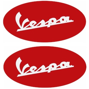 May include: Two red oval stickers featuring the white Vespa logo. The logo is a stylized script with the word "Vespa" in white, set against a solid red background. The stickers are likely for vehicles or merchandise.