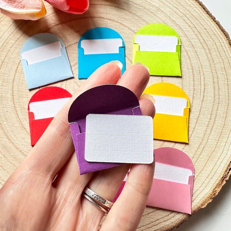 K&ouml;nnte beinhalten: Ein Satz von acht kleinen Umschl&auml;gen in verschiedenen Farben, darunter Lila, Rot, Gelb, Blau und Rosa. Jeder Umschlag hat eine wei&szlig;e Einlegekarte.