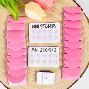 May include: Two sheets of pink mini stickers with a bow design. The stickers are packaged in pink envelopes. The text "MINI STICKERS" is printed on the sticker sheets.