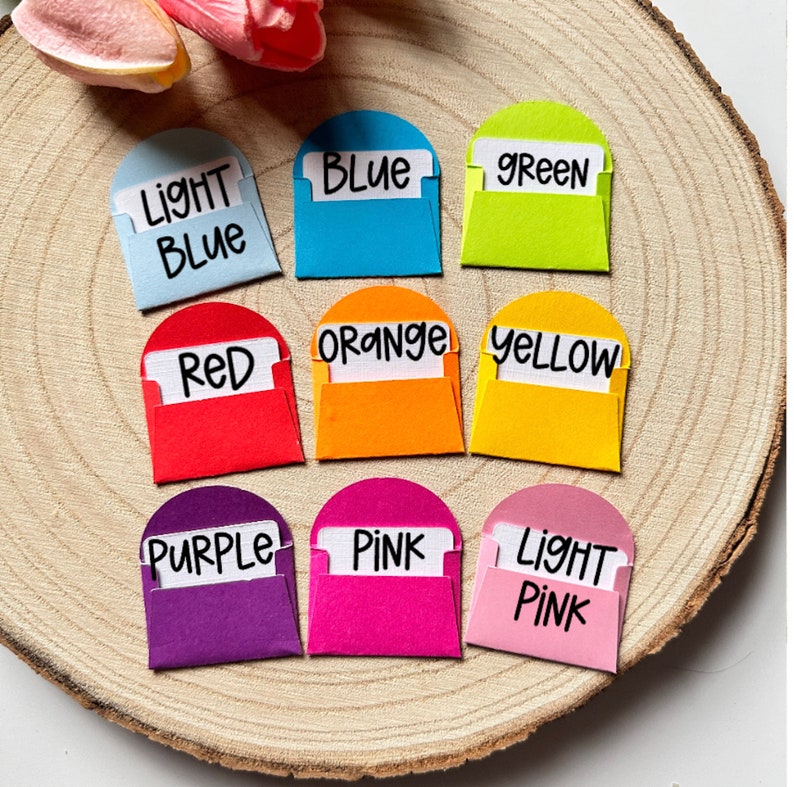 K&ouml;nnte beinhalten: Zehn kleine Umschl&auml;ge mit abgerundeten Oberseiten, jeder in einer anderen Farbe und mit dem Farbnamen in schwarzem Stift beschriftet. Die Farben sind hellblau, blau, gr&uuml;n, rot, orange, gelb, lila, rosa und hellrosa.