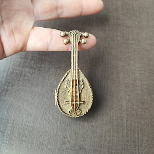 May include: A gold-toned metal musical instrument shaped like a lute with intricate details. The instrument has a hinged lid and is a decorative piece.