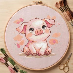 Peut inclure: Broderie au point de croix d'un adorable porcelet rose, avec de grands yeux et un sourire, dans un cercle à broder en bois. Le motif présente des accents roses et pêche. Fils à broder et ciseaux sont également visibles.
