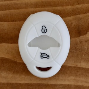 May include: White silicone key fob cover with a car icon and a lock icon. The cover has a cutout for the key and a hole for the key ring.