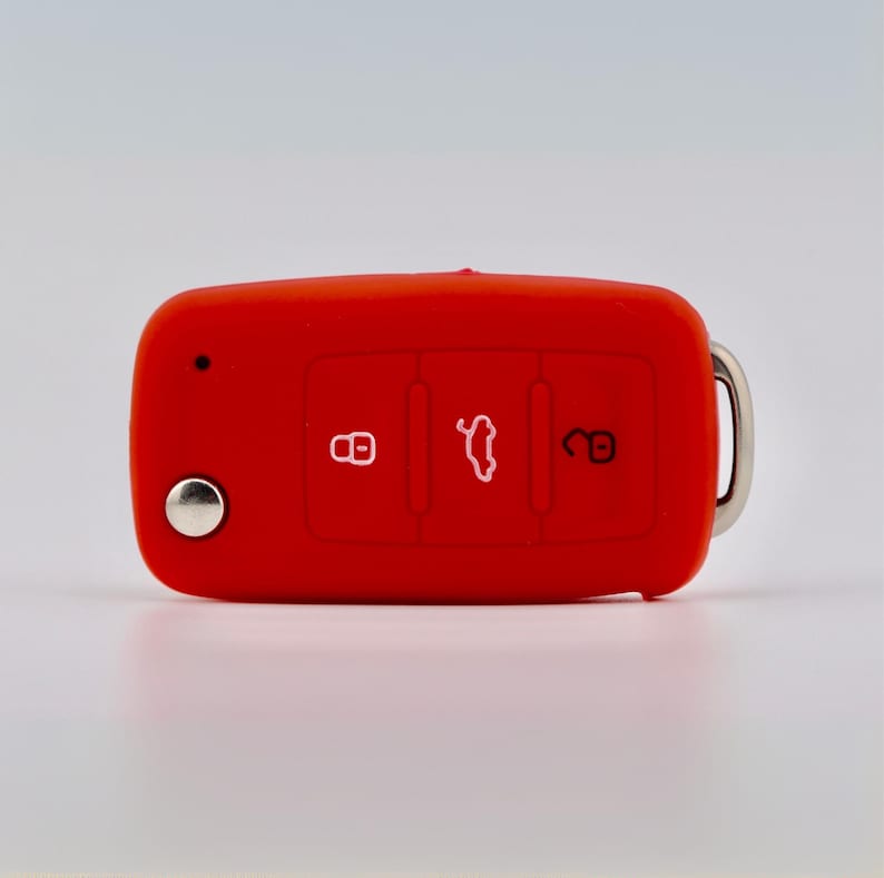 May include: A bright red silicone car key fob cover featuring three embossed icons: a locked padlock, a car trunk symbol, and an unlocked padlock. The cover includes a circular silver metal button on the left side and a silver metal ring on the right.