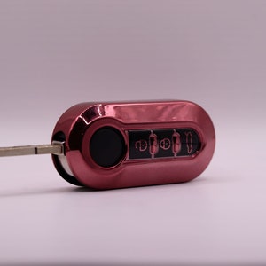 Puede incluir: Una llave de coche roja con una hoja de llave plateada y cuatro botones. Los botones tienen s&iacute;mbolos para desbloquear, bloquear, abrir el maletero y p&aacute;nico.