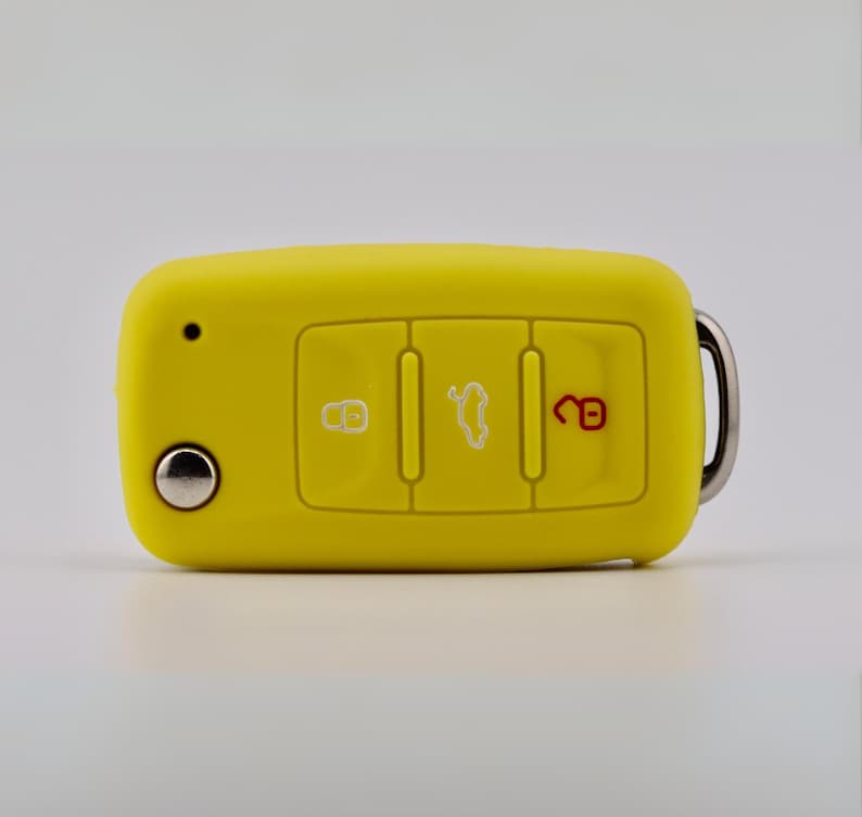 May include: A bright yellow silicone car key fob cover featuring three rectangular buttons. The left button displays a white lock icon, the center button shows a white car trunk icon, and the right button features a red unlocked padlock icon.