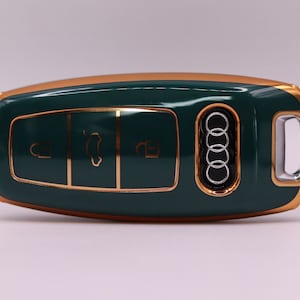 Puede incluir: Una llave de coche verde y dorada con cuatro botones y el logotipo de Audi.