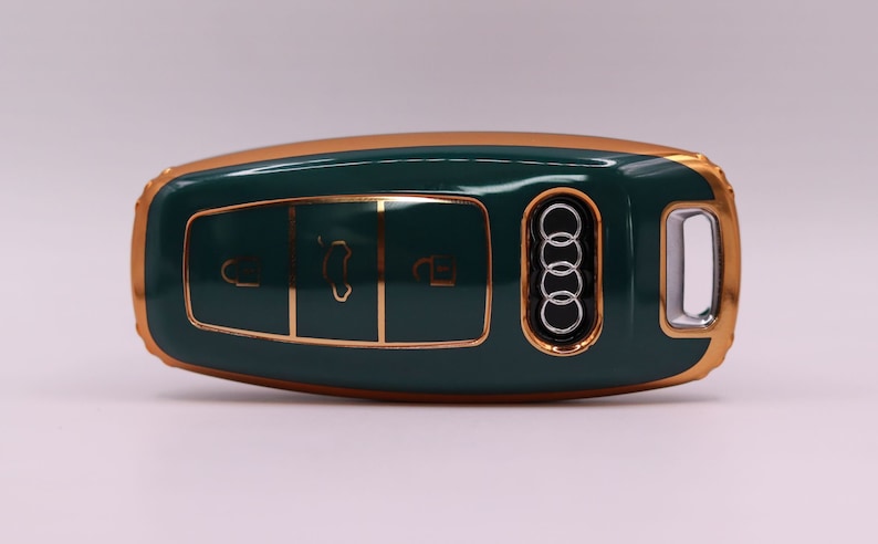 Puede incluir: Una llave de coche verde y dorada con cuatro botones y el logotipo de Audi.