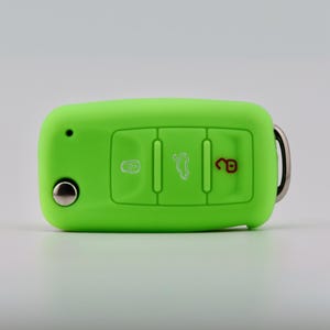 May include: A bright lime green silicone car key fob cover featuring three embossed button icons. The left icon is a white lock, the center icon is a white trunk release, and the right icon is a red unlock symbol. A silver metal ring is attached.