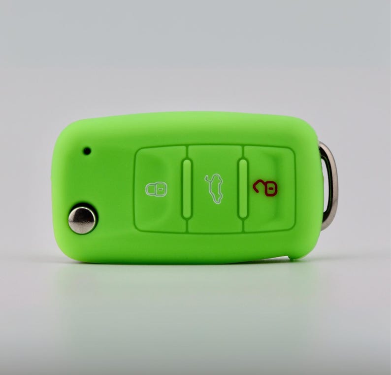 May include: A bright lime green silicone car key fob cover featuring three embossed button icons. The left icon is a white lock, the center icon is a white trunk release, and the right icon is a red unlock symbol. A silver metal ring is attached.