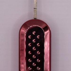 Puede incluir: Una llave de coche roja con una hoja de llave plateada y un dise&ntilde;o de media luna en el llavero.