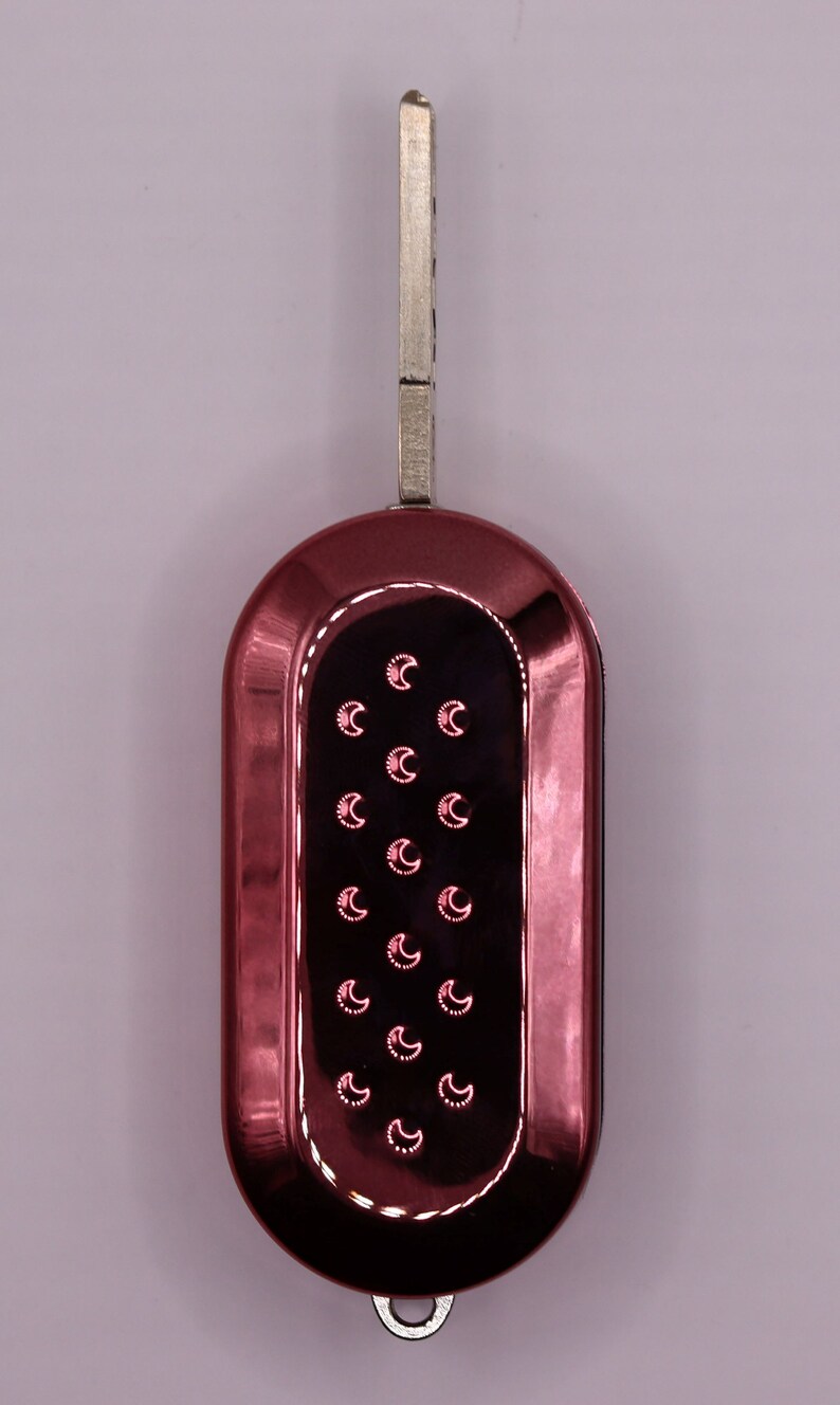 Puede incluir: Una llave de coche roja con una hoja de llave plateada y un dise&ntilde;o de media luna en el llavero.