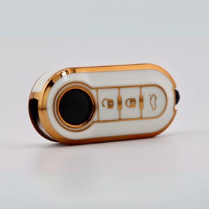 May include: A white car key fob with gold trim and black buttons. The key has three buttons with key, lock, and trunk icons. The key is oval-shaped and has a gold border.