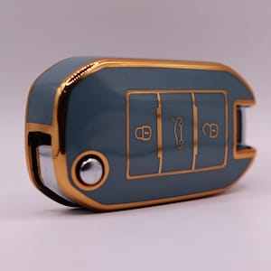 Puede incluir: Una llave de coche gris con ribetes dorados y tres botones. Los botones tienen iconos para bloquear, desbloquear y abrir el maletero.