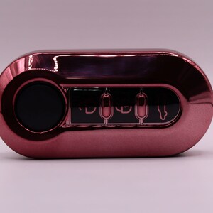 Puede incluir: Un llavero de coche de color oro rosa con cuatro botones y una cerradura negra. El llavero tiene un anillo plateado para sujetarlo a un llavero.