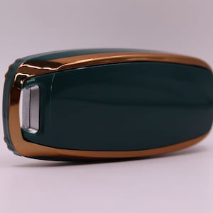 Puede incluir: Un llavero verde oscuro con ribete dorado. El llavero tiene un peque&ntilde;o bot&oacute;n rectangular en el lateral.