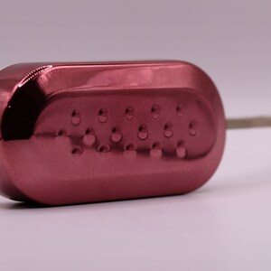 Puede incluir: Una llave de coche roja con una hoja de llave plateada. La llave tiene una superficie texturizada con peque&ntilde;as hendiduras circulares.
