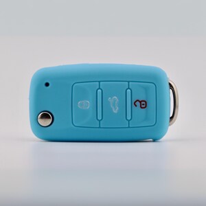 May include: A light blue silicone car key fob cover featuring three embossed buttons. The left button shows a locked padlock icon, the center button displays a car trunk icon, and the right button features an unlocked red padlock icon.