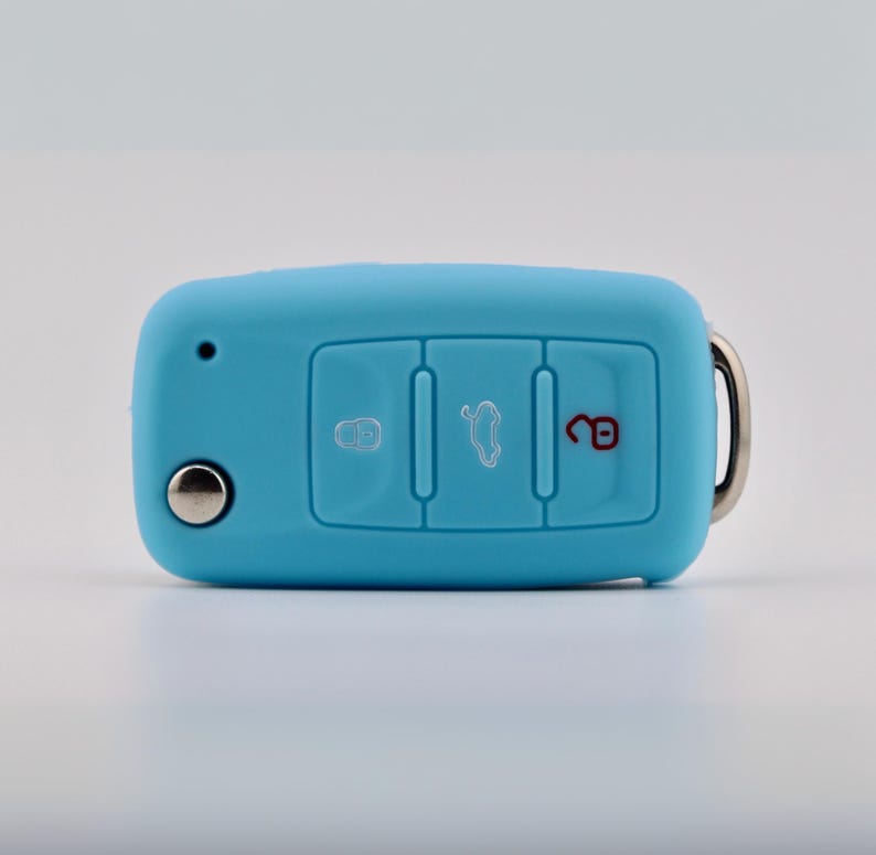 May include: A light blue silicone car key fob cover featuring three embossed buttons. The left button shows a locked padlock icon, the center button displays a car trunk icon, and the right button features an unlocked red padlock icon.