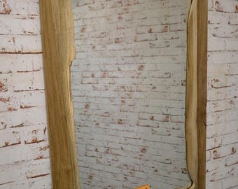 Könnte beinhalten: Rechteckiger Spiegel mit einem Rahmen aus Naturholz. Der Rahmen hat ein einzigartiges, wellenförmiges Kantendesign. Der Spiegel ist an einer weißen Backsteinmauer befestigt. Ein kleiner orangefarbener Aufkleber mit der Nummer 78 ist sichtbar.