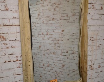Könnte beinhalten: Ein rechteckiger Spiegel mit einem Naturholzrahmen. Der Rahmen hat ein einzigartiges, wellenförmiges Kantendesign. Der Spiegel wird vor einer weißen Backsteinmauer gezeigt. Ein kleines orangefarbenes Etikett mit der Nummer 79 ist sichtbar.