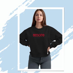 Könnte beinhalten: Ein schwarzer Pullover mit dem Wort "amore" in Rot auf der Vorderseite gestickt.