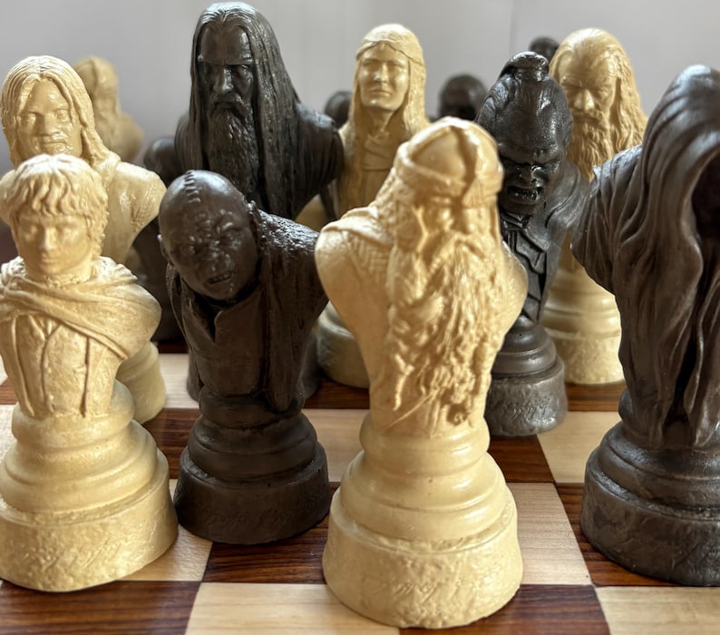 May include: A detailed chess set featuring character busts in shades of beige and dark brown. The chess pieces are arranged on a wooden checkered board, showcasing intricate details and varying textures.