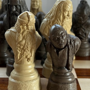 May include: A detailed chess set featuring character busts in various colors. The pieces include figures with long beards and detailed facial features. The set is displayed on a checkered wooden board, showcasing the intricate design of each piece.