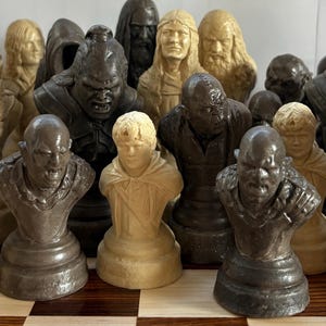 May include: A collection of chess pieces, each sculpted as a bust of a character. The pieces are in shades of cream and brown, with detailed facial features and attire. The set appears to be themed after a fantasy series.