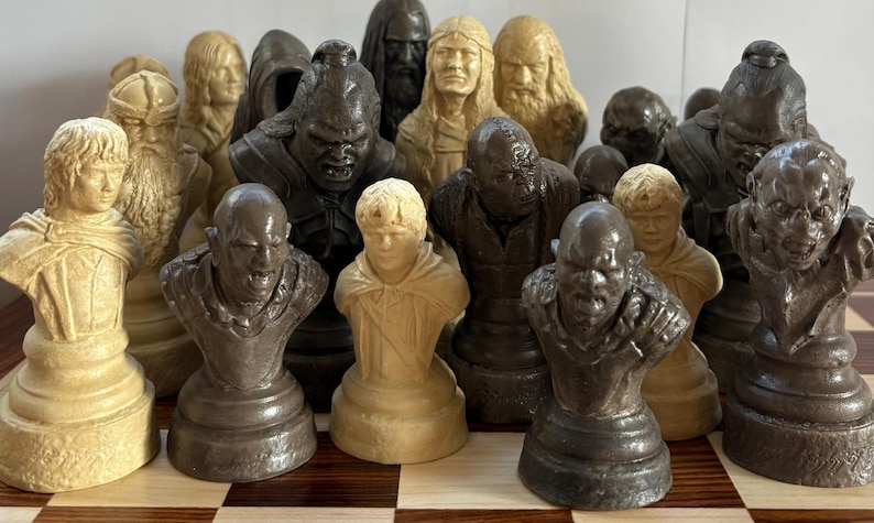 May include: A collection of chess pieces, each sculpted as a bust of a character. The pieces are in shades of cream and brown, with detailed facial features and attire. The set appears to be themed after a fantasy series.