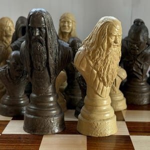 May include: A chess set featuring intricately carved busts of figures with long hair and beards. The pieces are in shades of brown and tan, set on a checkered wooden board. The pieces are detailed and appear to be themed.