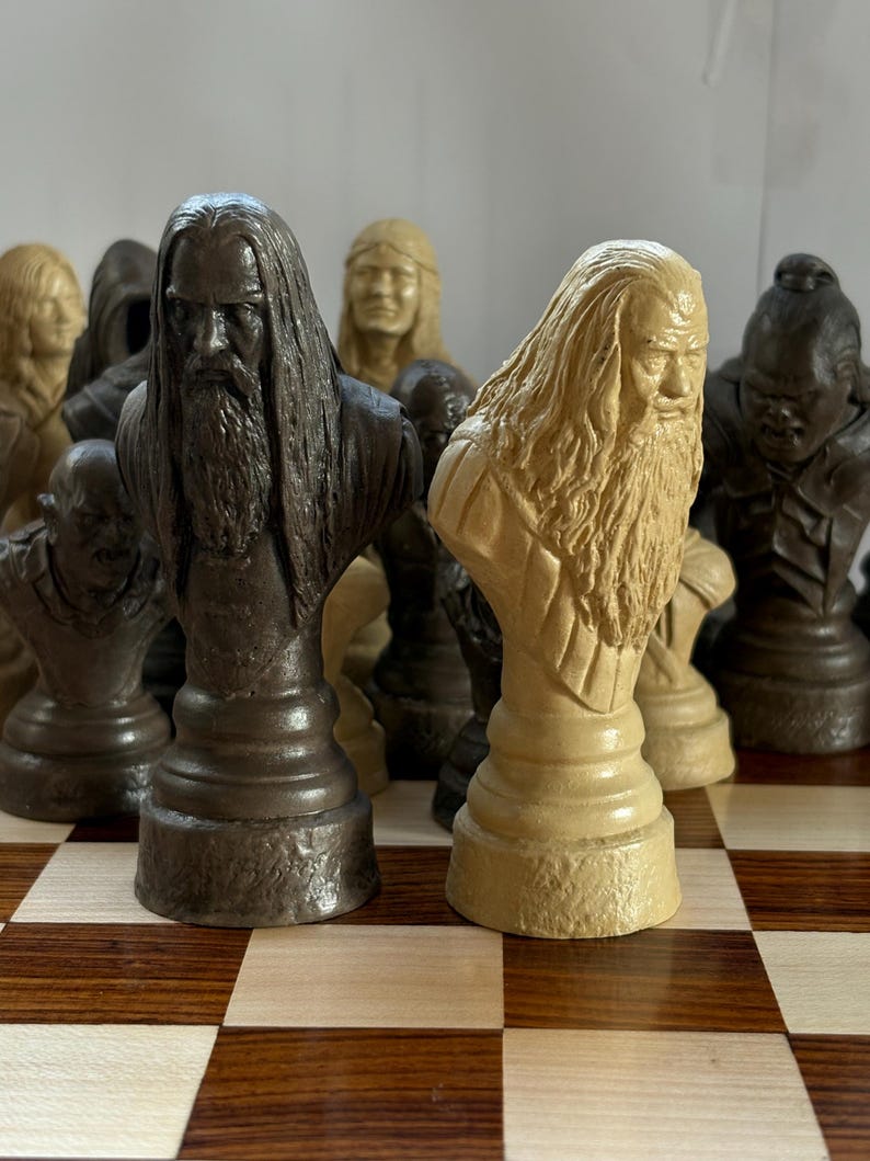 May include: A chess set featuring intricately carved busts of figures with long hair and beards. The pieces are in shades of brown and tan, set on a checkered wooden board. The pieces are detailed and appear to be themed.