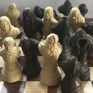 May include: A chess set featuring detailed bust-shaped pieces in shades of black and cream. The chess pieces are arranged on a checkered board. The pieces appear to be inspired by a fantasy theme.