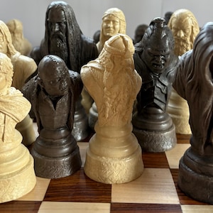 May include: A detailed chess set featuring character busts in shades of beige, brown, and black. The pieces are arranged on a checkered board, showcasing intricate details and varying heights. The set appears to be themed, with each piece representing a different character.