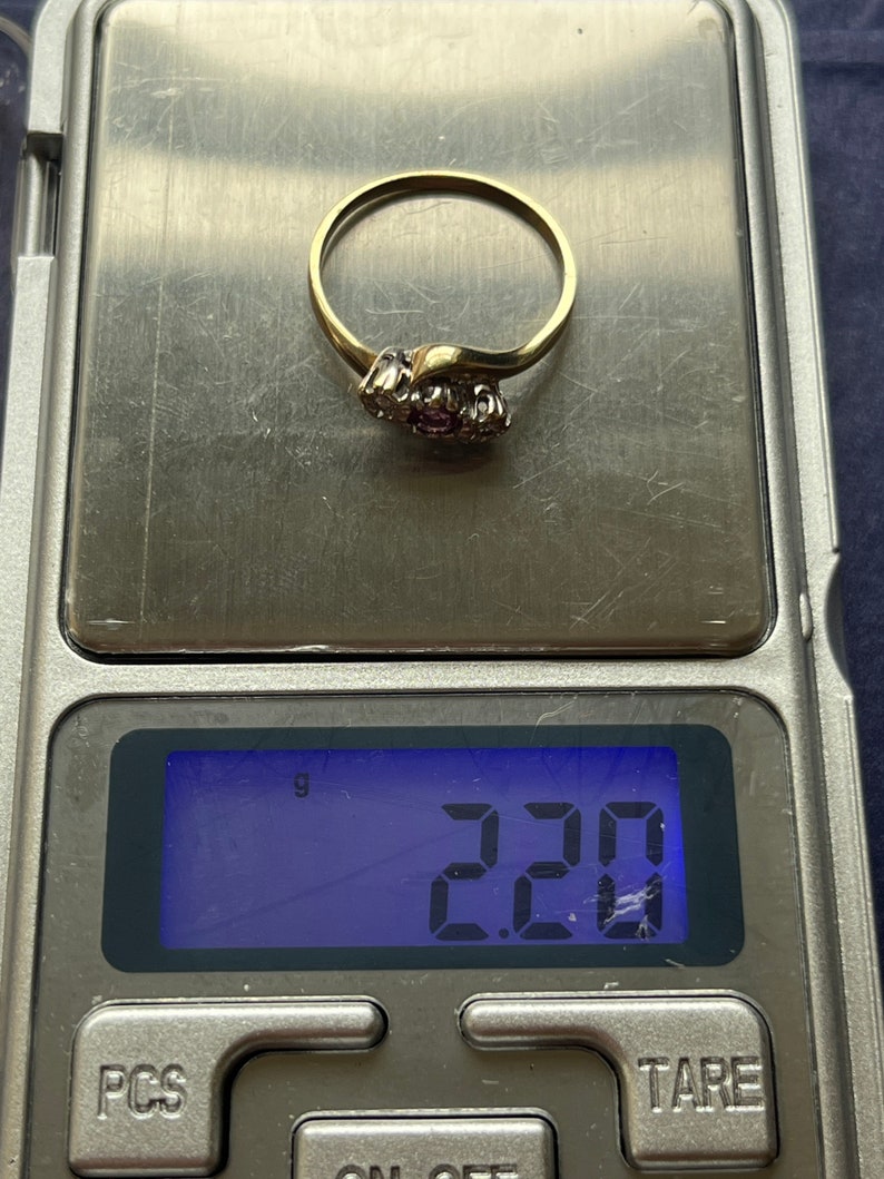 以下が含まれることがあります： 小さな丸い宝石のクラスターが付いたゴールドリング。 リングはデジタルスケール上にあり、2.20グラムの重量が表示されています。 リングは繊細で湾曲したデザインです。