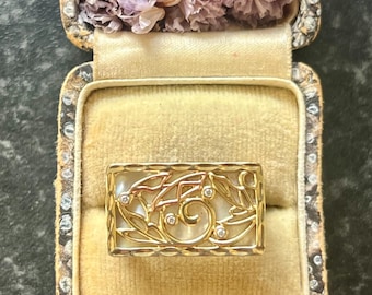 May include: A rectangular gold ring with a mother-of-pearl inlay and a filigree design featuring leaves and small diamonds. The ring is displayed in an antique jewellery box with dried flowers.