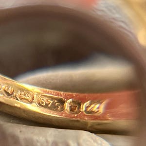 以下が含まれることがあります： 金色の指輪のクローズアップ。刻印が見えます。指輪のバンドは滑らかで磨かれており、「375」の数字が刻印されており、金の純度を示しています。指輪はおそらくジュエリーです。