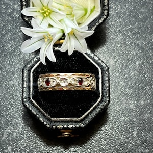 May include: A gold ring with three red gemstones and white diamonds set in a decorative band. The ring is in a black velvet ring box.