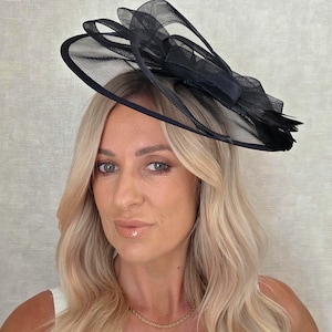 May include: A black formal hat with a mesh design and a bow. The hat is worn on the head. The hat is made of a lightweight material and is suitable for special occasions.