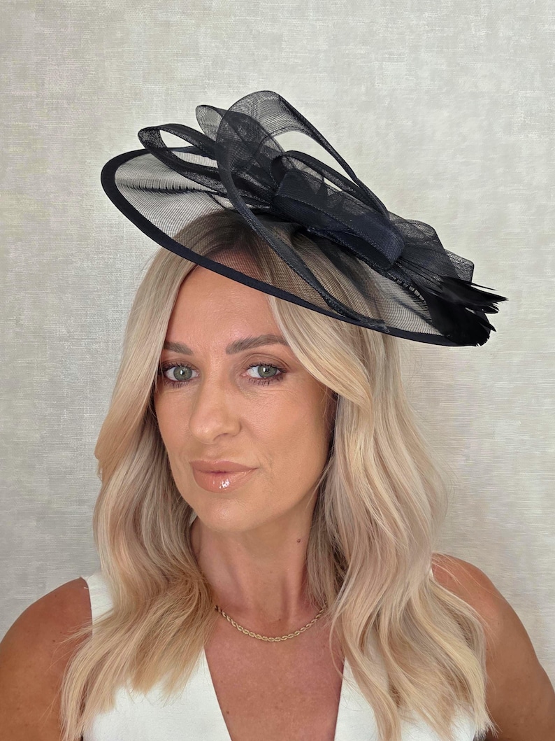 May include: A black formal hat with a mesh design and a bow. The hat is worn on the head. The hat is made of a lightweight material and is suitable for special occasions.