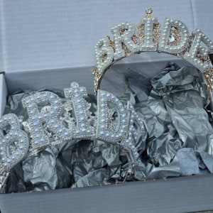 May include: Two gold-tone 'Bride' headbands with white pearl embellishments. The headbands are in a white box with tissue paper.