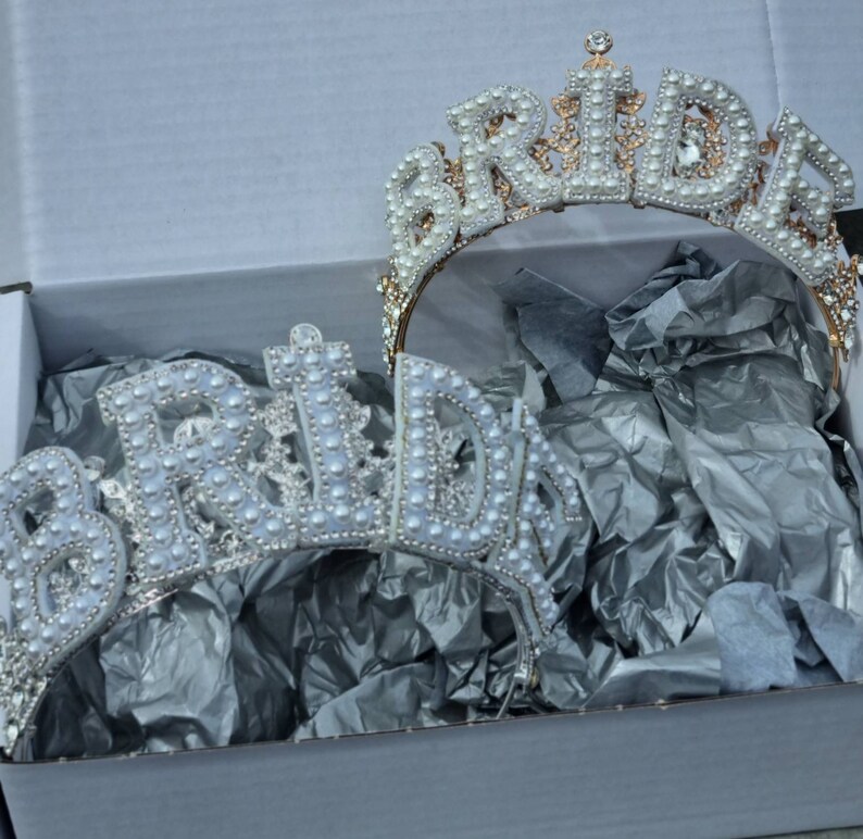 May include: Two gold-tone 'Bride' headbands with white pearl embellishments. The headbands are in a white box with tissue paper.
