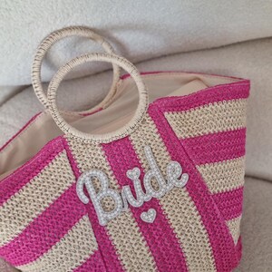 May include: Pink and beige striped straw tote bag with a white beaded "Bride" embellishment.
