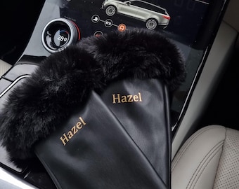 May include: A pair of black leather gloves with faux fur cuffs. The gloves have the name "Hazel" embroidered on the back in gold thread.