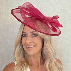 May include: A magenta-colored hat with a wide brim and a decorative bow made of sheer fabric. The hat features a dark red trim and is adorned with feathers. This formal headwear is suitable for special occasions.